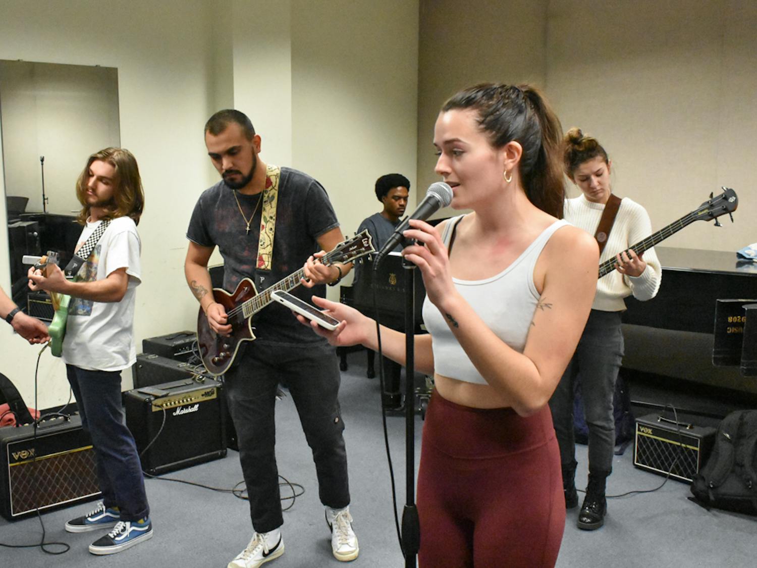 Coordinator and instructor of music industry studies Jeremy Polley (far left) changes third-year music industry studies student Harry Milvid’s guitar settings while second-year music industries student Megan Gallagher (right) is pictured singing “Santeria” by Sublime. Gallagher sings for the ensemble and arranges music for an acapella group. She uses music to communicate her emotions and believes in “the power that (music) can have mentally over your emotions.”