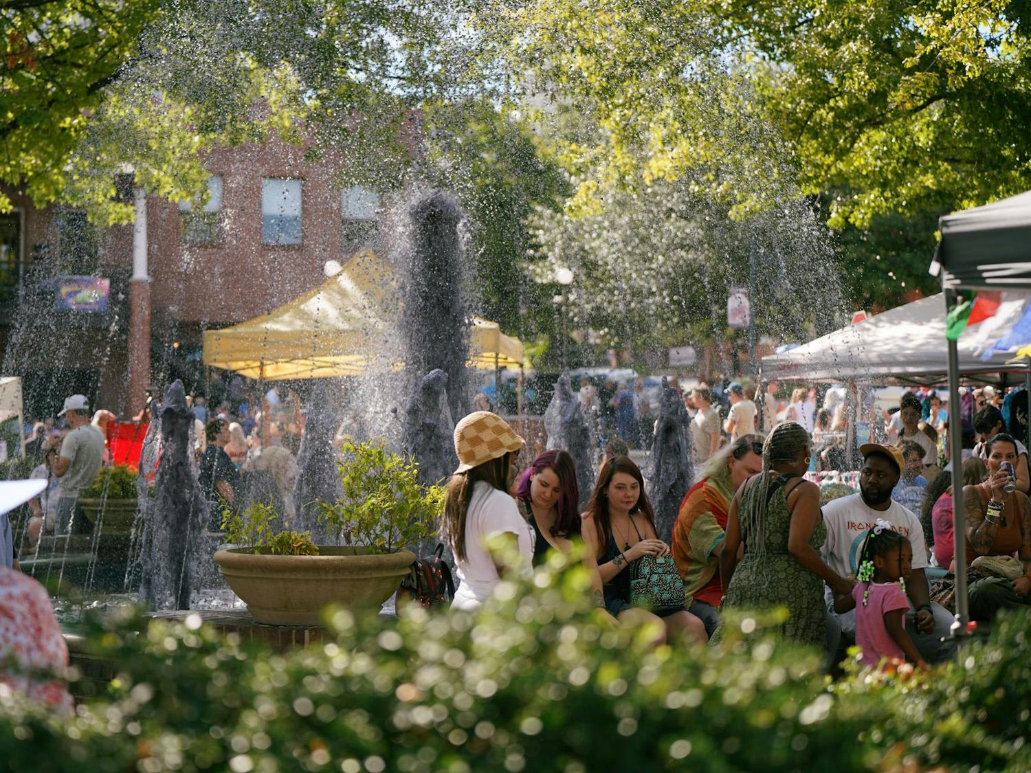Festivalgoers relax in the shade by a purple-toned fountain on Oct. 1, 2023. The tents featured in the background housed local businesses that sold everything from food to clothing. 