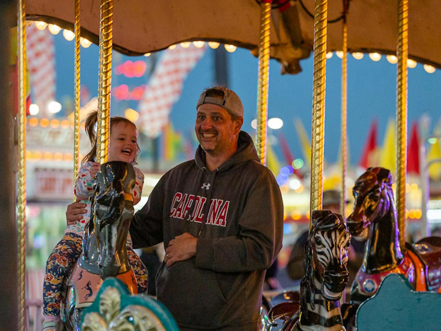 Columbia residents 2-year-old Abby Malizia (on left) and her father, 40-year-old Kevin Malizia (on right) ride a merry-go-round at the South Carolina State Fair on Oct.18, 2022. The S.C. State Fair features a variety of both high-energy and relaxing rides for fair attendees of all ages.