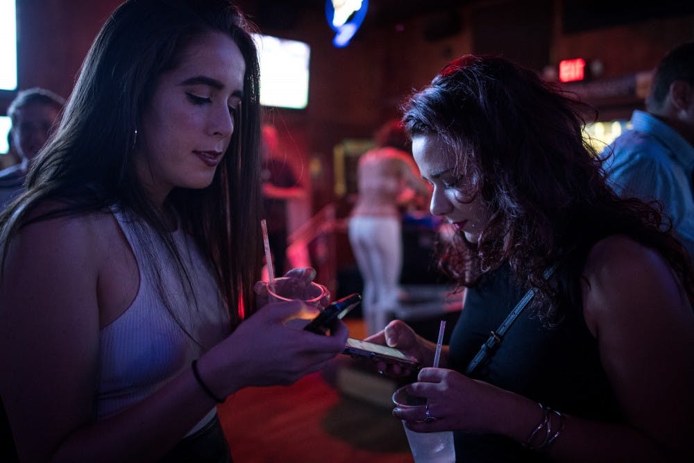 Star Tribune reporters Natalie Daher and Danielle Fox check their Tinder notifications and messages while waiting near the entrance of Sneaky Pete's before their first Tinder Social dates late Saturday night, Aug. 6, 2016 in Minneapolis.  (Aaron Lavinsky/Minneapolis Star Tribune/TNS) 