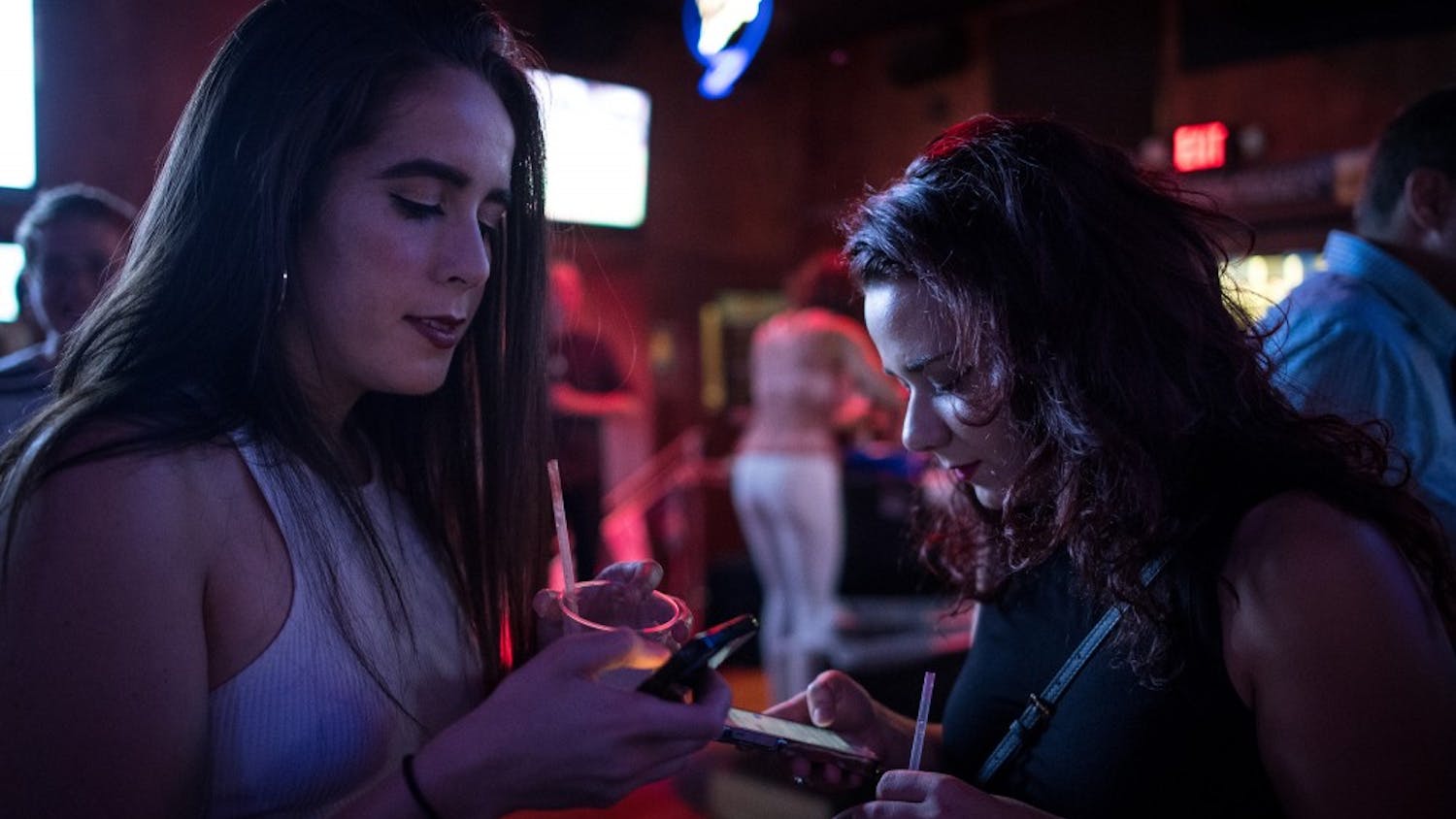 Star Tribune reporters Natalie Daher and Danielle Fox check their Tinder notifications and messages while waiting near the entrance of Sneaky Pete's before their first Tinder Social dates late Saturday night, Aug. 6, 2016 in Minneapolis.  (Aaron Lavinsky/Minneapolis Star Tribune/TNS) 