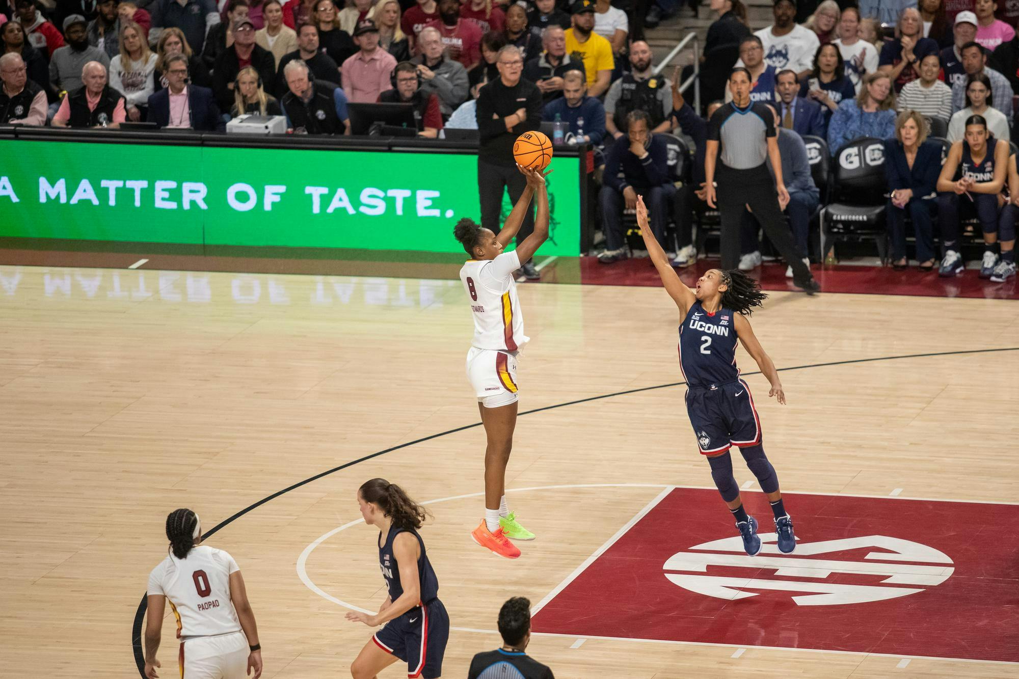 A player shoots the ball with another player jumping towards them. 