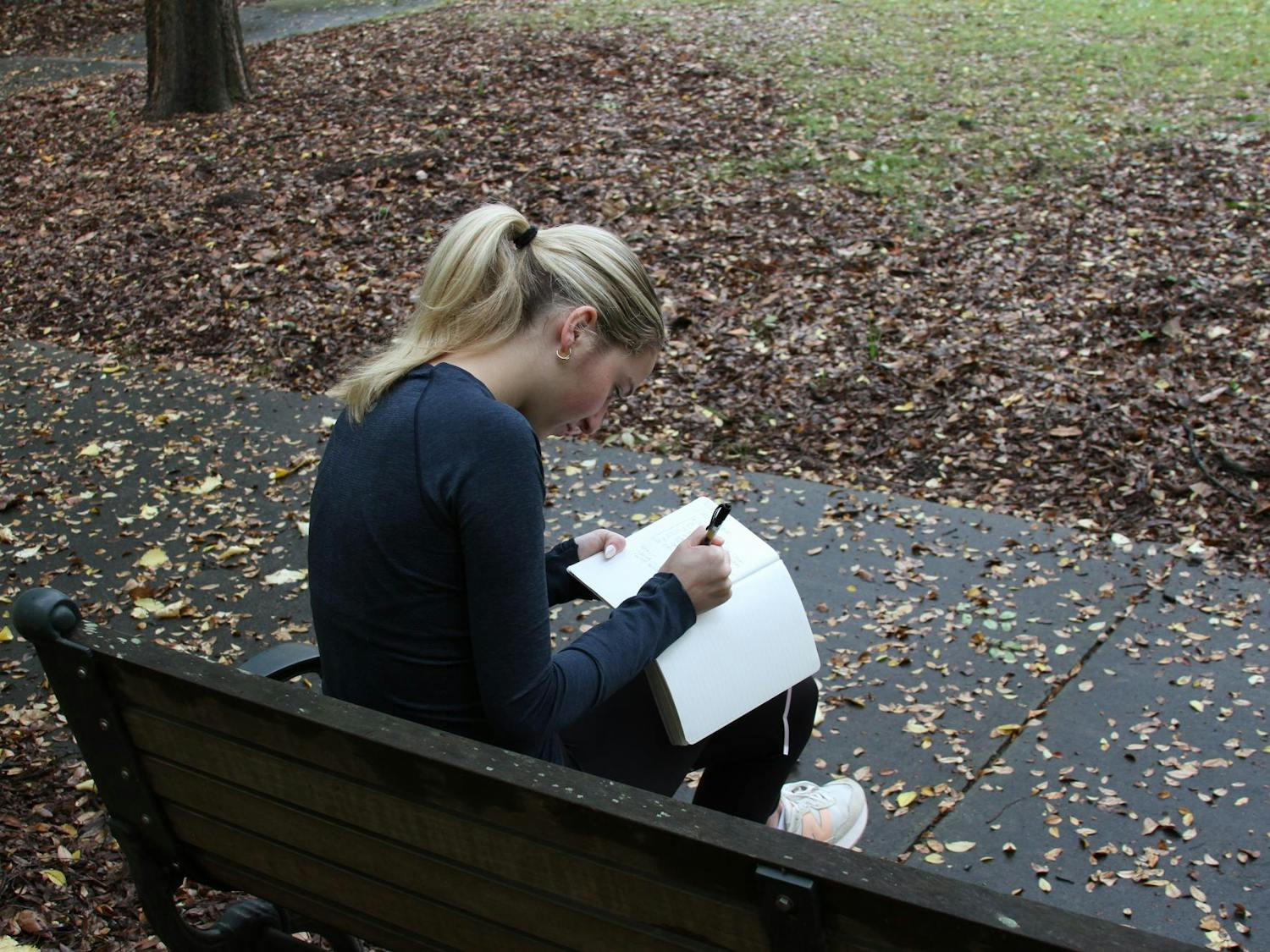 A photo illustration of a student sitting on a bench writing in their journal at the University of South Carolina on Nov. 11, 2024. Four times a year, Cassie Premo Steele invites writers to Congaree National Park for immersive workshops that blend nature walks with reflective journaling.
