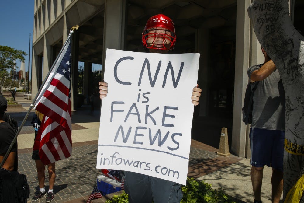 A man holding a sign that says, "CNN is Fake News" and "infowars.com" positioned himself into photos while the media covered an Impeachment March in downtown Los Angeles on July 2, 2017. (Jay L. Clendenin/Los Angeles Times/TNS)