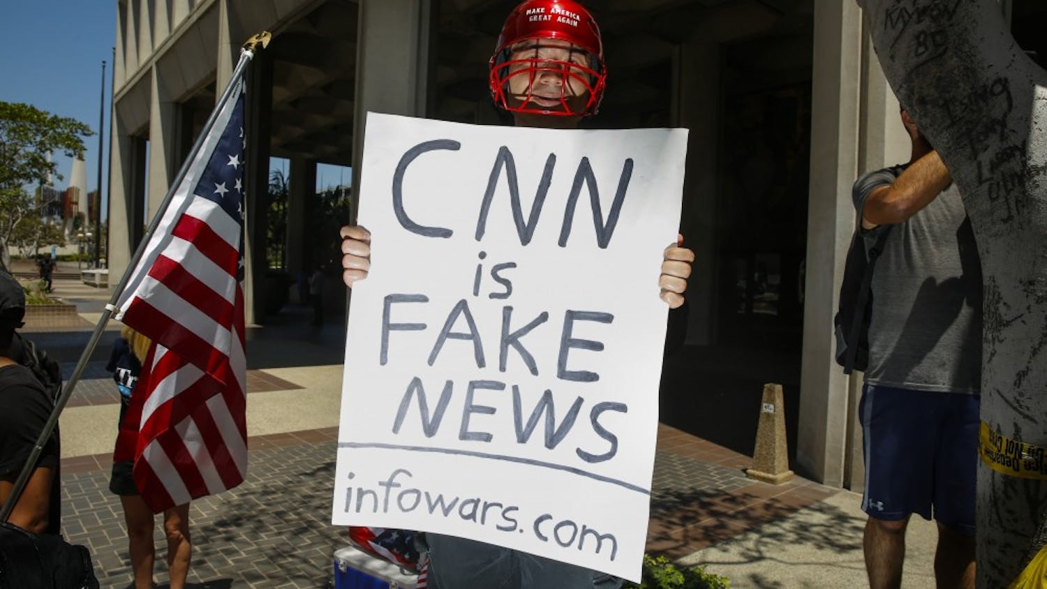 A man holding a sign that says, "CNN is Fake News" and "infowars.com" positioned himself into photos while the media covered an Impeachment March in downtown Los Angeles on July 2, 2017. (Jay L. Clendenin/Los Angeles Times/TNS)