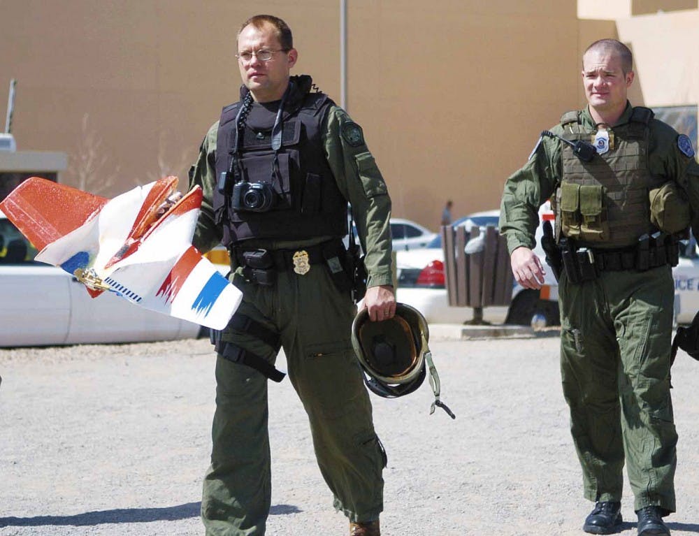 Albuquerque Police Department bomb squad technician Scott Smiel, left, carries the remote controlled airplane that crashed through a window at Johnson Center on Wednesday. A person was operating the toy plane, when winds knocked it into the building, auth