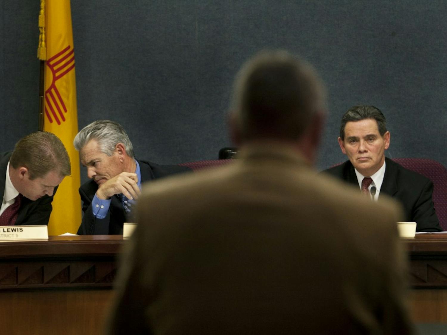 Dist. 5 Councilor Dan Lewis (left) talks to Brad Winter from Dist. 4 while Tim Cass, the UNM Senior Associate Athletics Director gives his remarks supporting UNM’s waiver to sell alcohol during football and basketball games at Monday’s city council meeting in the Vincent E. Griego chambers. The council denied the request by a 6-3 vote