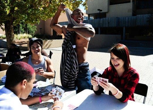 Thierry Milleret sheds a layer of clothing after losing a hand of strip poker Thursday in Smith Plaza. Milleret and, from left, Isaac Edwards, Louis Carter and Stephanie Turner participated in UNMPIRG's clothing drive, which continues today. 
