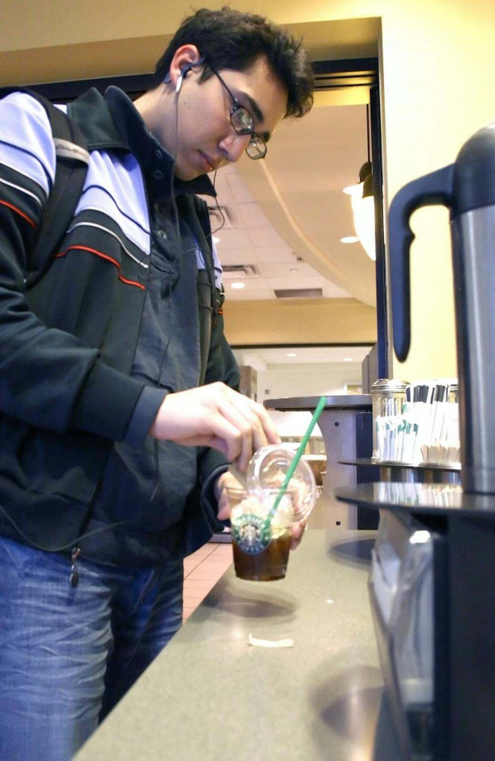 UNM student Julio Romero adds sugar to his iced espresso Tuesday outside of Starbucks at Zimmerman Library. Starbucks will open another coffee shop at Central Avenue and Terrace Street. It will be the fourth Starbucks within one mile of the University.