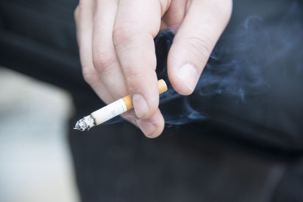 A student smokes outside Castetter Hall on Tuesday afternoon. UNM is considering a revision to the universitys smoking policy to include cracking down on smokers outside of designated smoking areas on campus.
