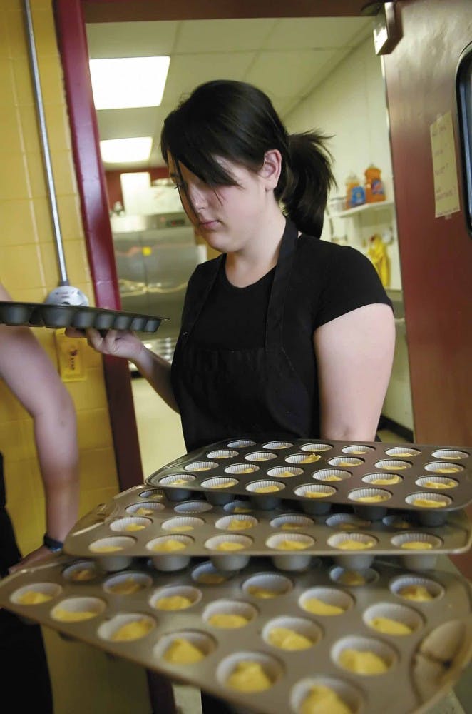 Keri Moore carries trays of cupcakes to put in the oven Monday at Cake Fetish.