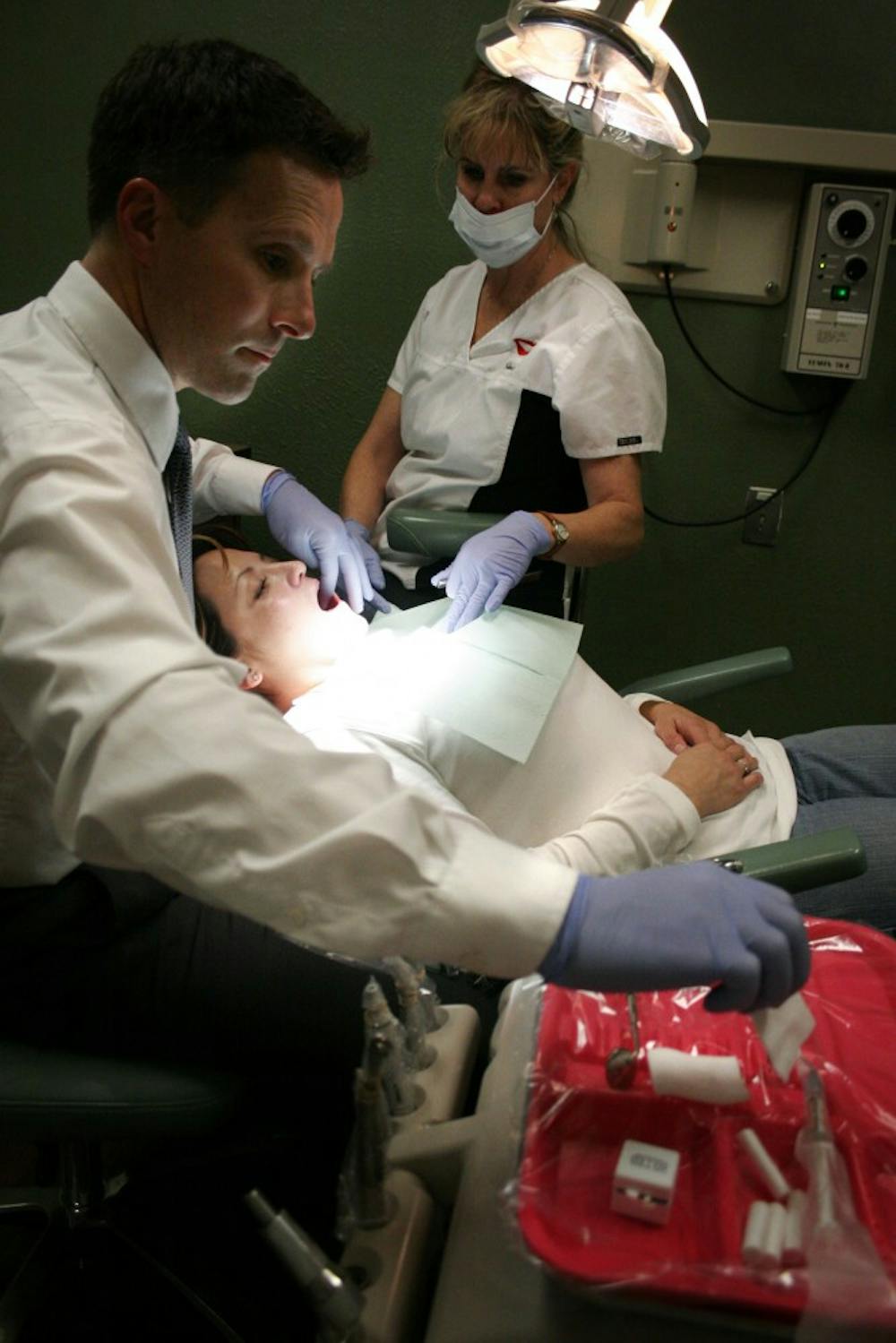 Dentist Mark Urbane, left, and assistant Chris Pulos examine Stephanie Sanchez's teeth Tuesday at his Albuquerque office.