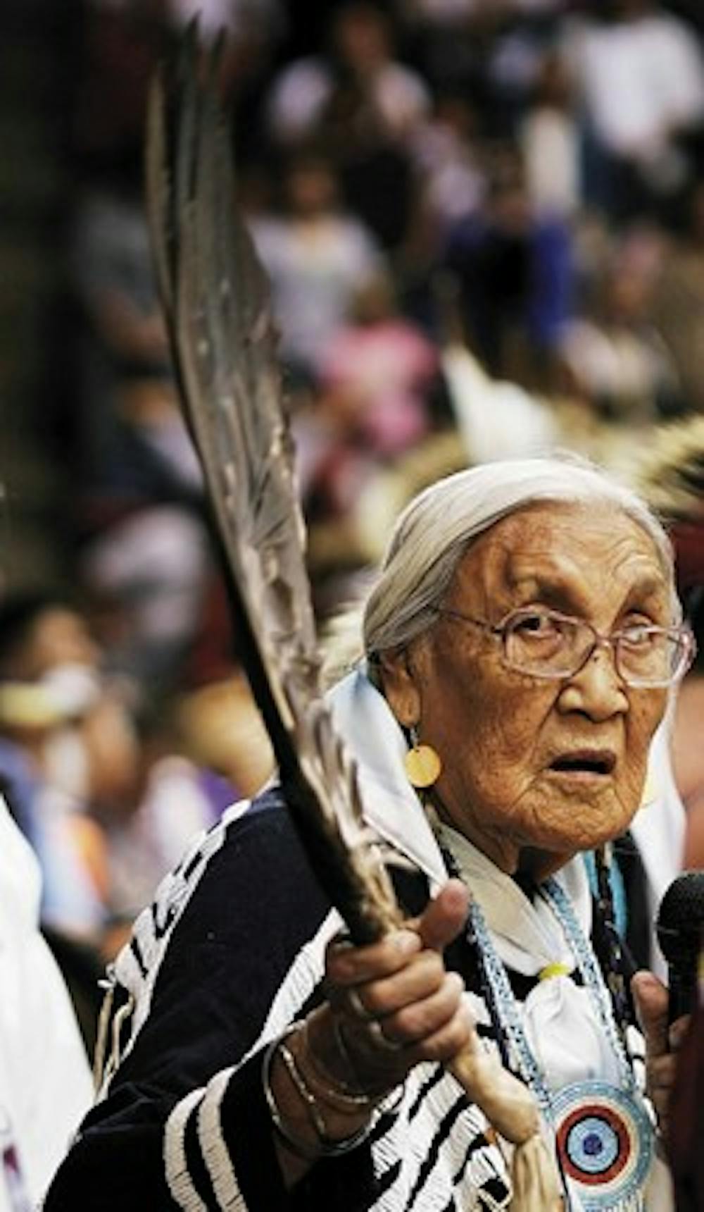 Elder Maggie Blackkettle waves an eagle feather over the crowd at The Pit on Saturday before the Gathering of Nations Powwow dancers' grand entrance.