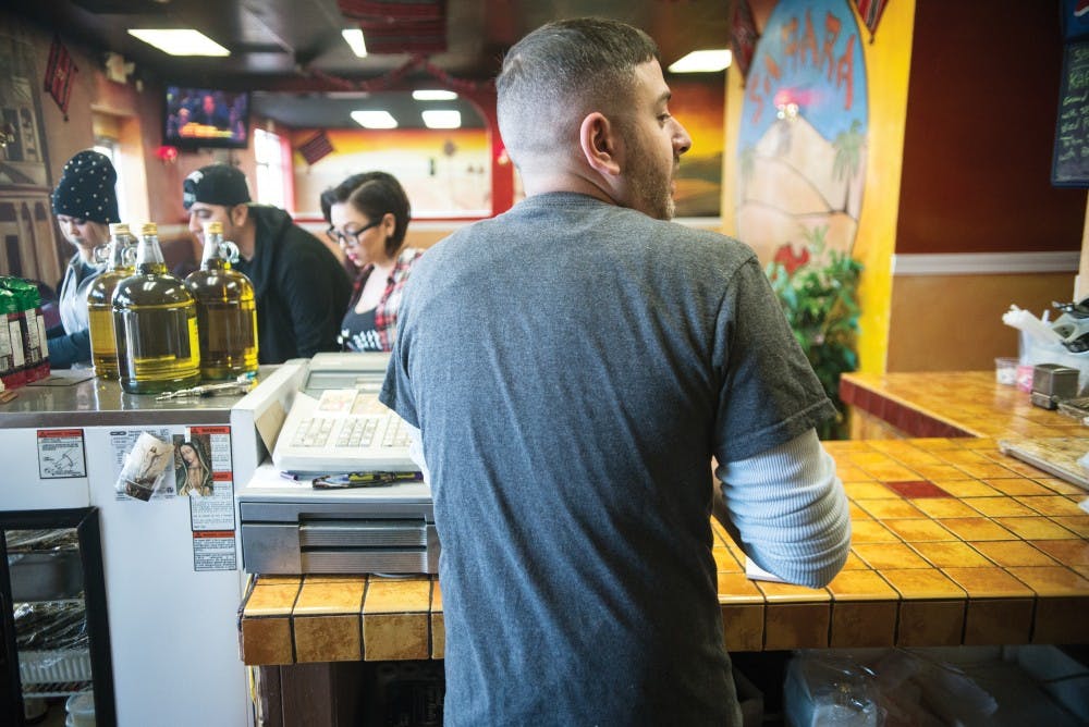 Co-owner of Sahara Middle Eastern Eatery Omar Nesheiwat calls out an order as customers look at a drink cooler Wednesday afternoon at their central location. Nesheiwat takes orders for customers, cooks and prepares food during his shift.