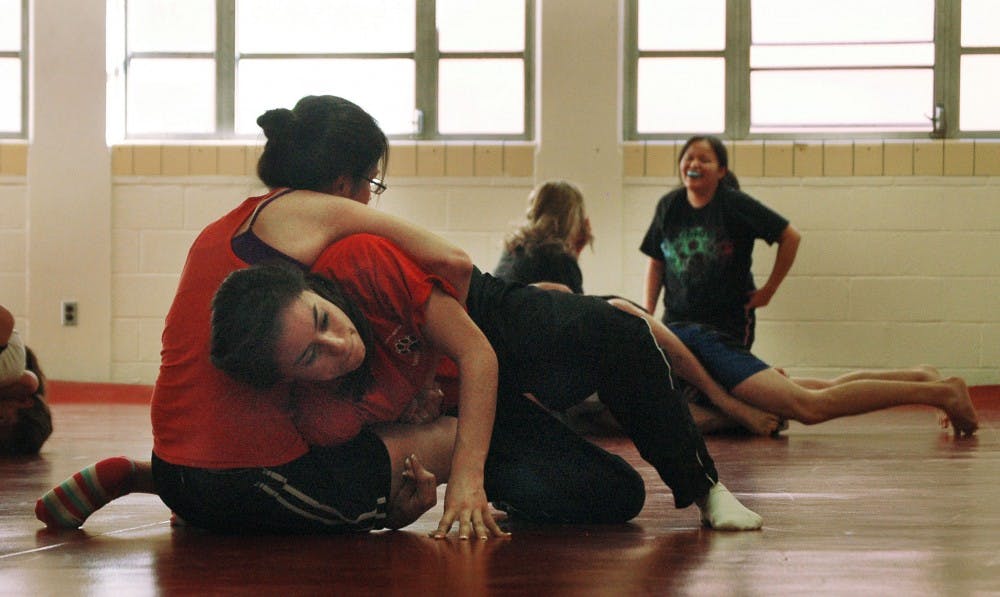 	Rebeca Gurrola, right, and Claudia DeSantiago practice takedowns in their personal defense class in Johnson Gym Thursday. The Women’s Resource Center is offering a personal defense class Monday in response to the Feb. 15 student stabbing.