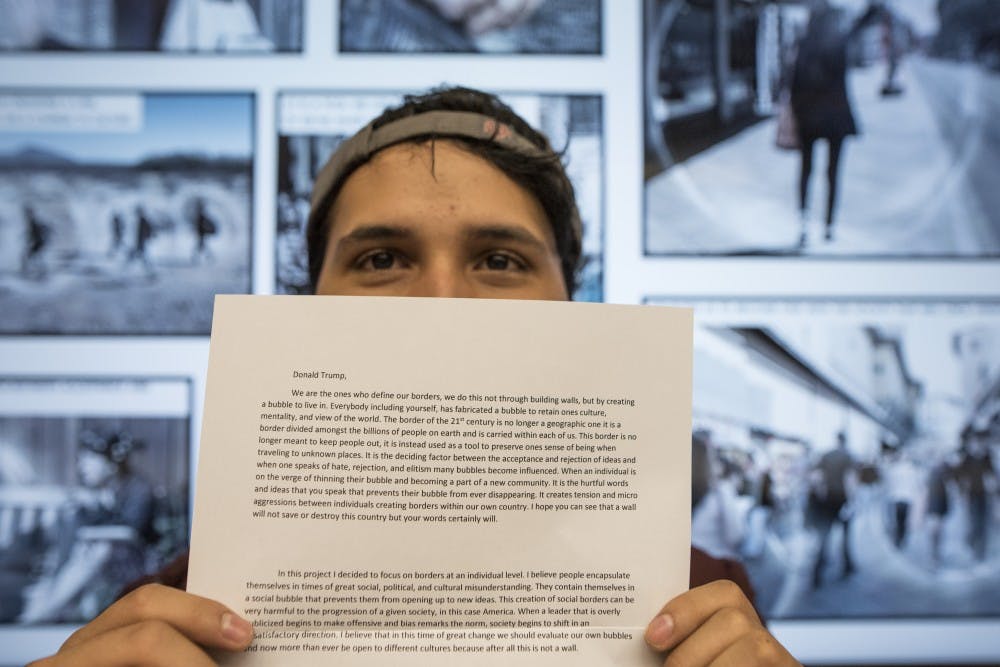 A UNM Architecture and Planning students stands in front of his proposed boarder wall while holding a letter to President Donald Trump Wednesday, April 26, 2017 at George Pearl Hall. Students where tasked with designing their own rendition of a United States Mexico boarder wall and to write a letter to Trump critiquing current policies.