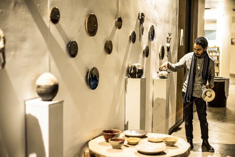 Miguel Lastra adjusts a piece of Raku-fired figural sculptures and Rake gas reduction fired functional vessels on the wall as part of a collaborative art gallery titled “Figure Function Time.”