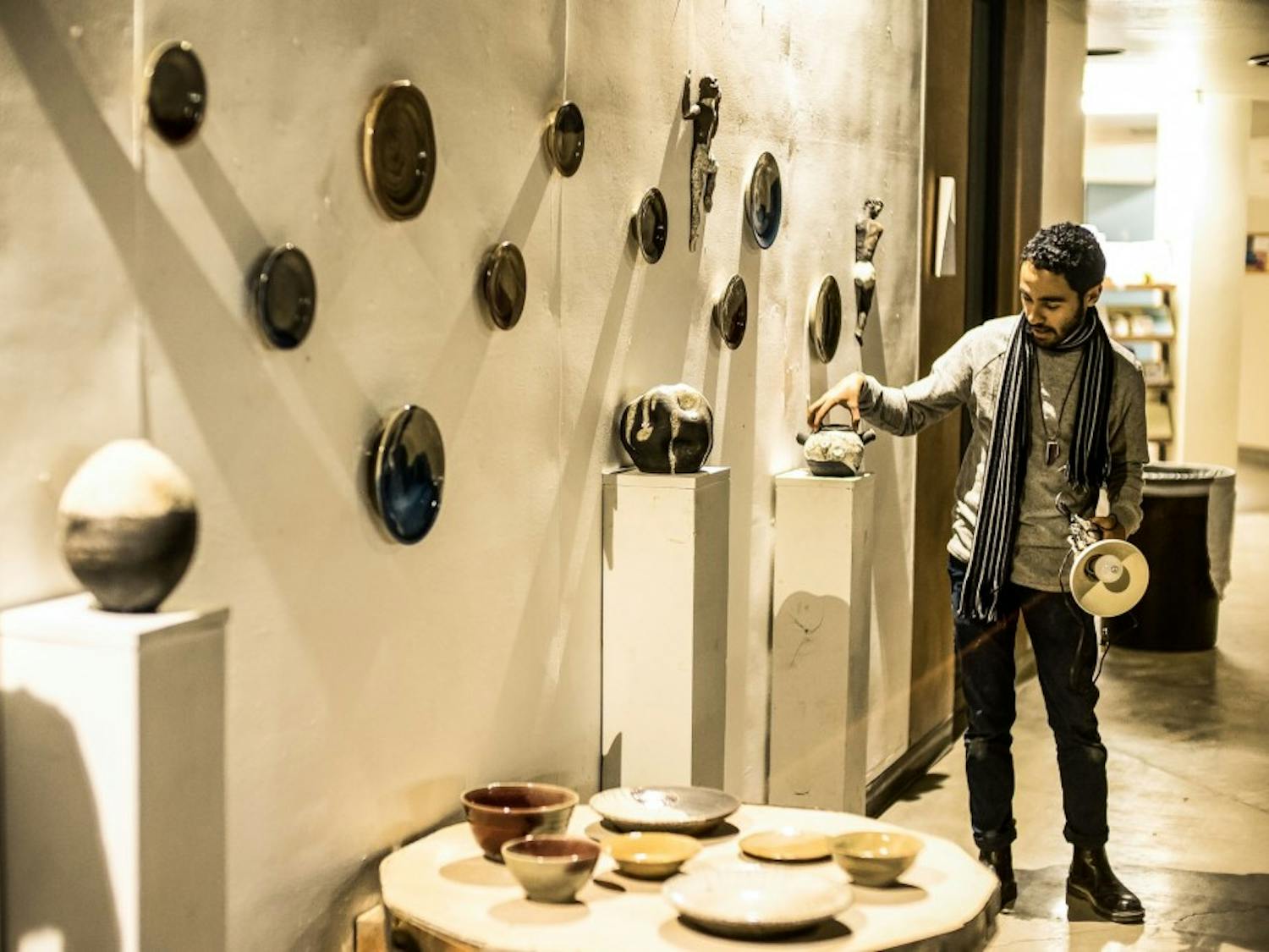 Miguel Lastra adjusts a piece of Raku-fired figural sculptures and Rake gas reduction fired functional vessels on the wall as part of a collaborative art gallery titled “Figure Function Time.”