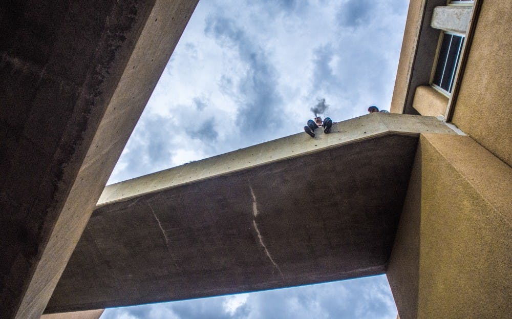 A UNM student smokes while sitting on the ledge of a main campus building Wednesday, August 23rd 2017. The instituted "tobacco-free campus" campaign has led to a phasing out of designated smoking areas for students, residents and faculty across campus.