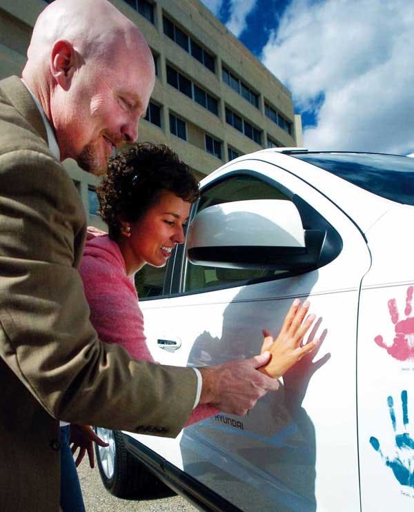 Tom Hornbeck helps Carmen Martinez make a handprint on a Hyundai Santa Fe as part of the Hope on Wheels Tour at the Cancer Research Center on Wednesday. There are six Hyundai vehicles traveling across the country that will be donated to pediatric cancer r