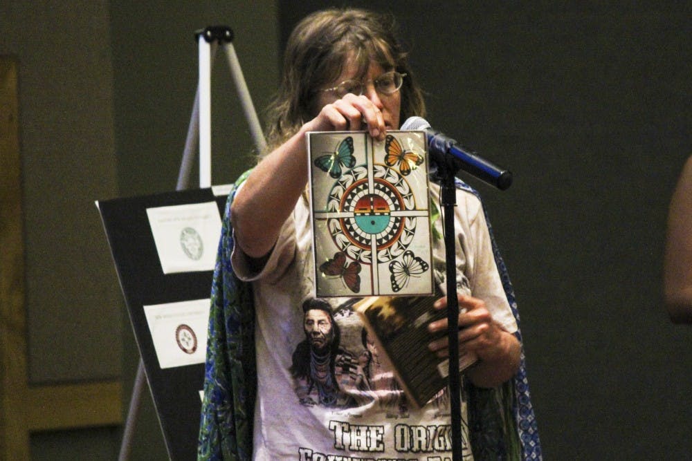 Deborah Gaudet holds up artwork by artist Jason Valencia of San Felipe Pueblo Thursday afternoon at the SUB Ballroom. Gaudet was one of many who voiced their opinions and ideas on changing UNM’s seal.