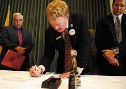 Patrick Lyons, New Mexico commissioner of public lands, signs a patent for a plot of land for a UNM campus in Rio Rancho on Monday in the SUB. Jamie Koch, president of the Board of Regents, left, and Bob Stranahan, general councilor of the State Land Offi