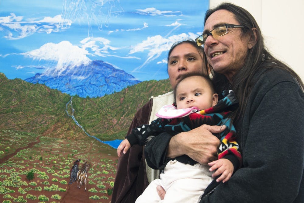 Jimmy Lujan, right, and his wife Shawna Sandoval embrace their 5-month-old Akiya in front of Lujan’s painting, “Guardians of Stolen Love,” at Albuquerque Health Care for the Homeless on Wednesday. Lujan was once one of many experiencing homelessness in Albuquerque and started his recovery participating in ArtStreet at AHCH, a program through which people can make art free of charge and even sell it.