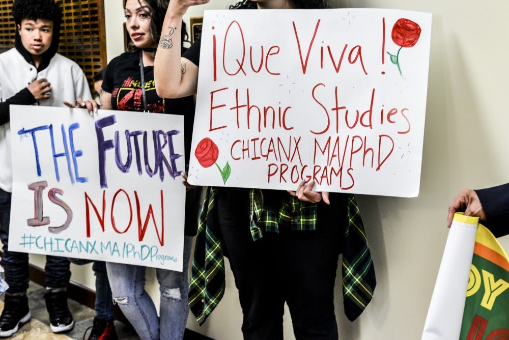 Two demonstrators hold signs to show their support of adding a master's, master's certificate and doctoral degree program to the Chicana and Chicano Studies Department on April 24, 2018 . The Faculty Senate unanimously passed the proposal.