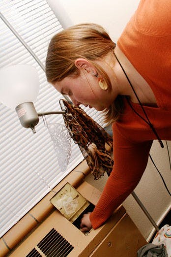 Student Blaise Threet adjusts her heater in Coronado Hall on Monday. Students say the dorms are too warm now that the cooling system has been switched off. 