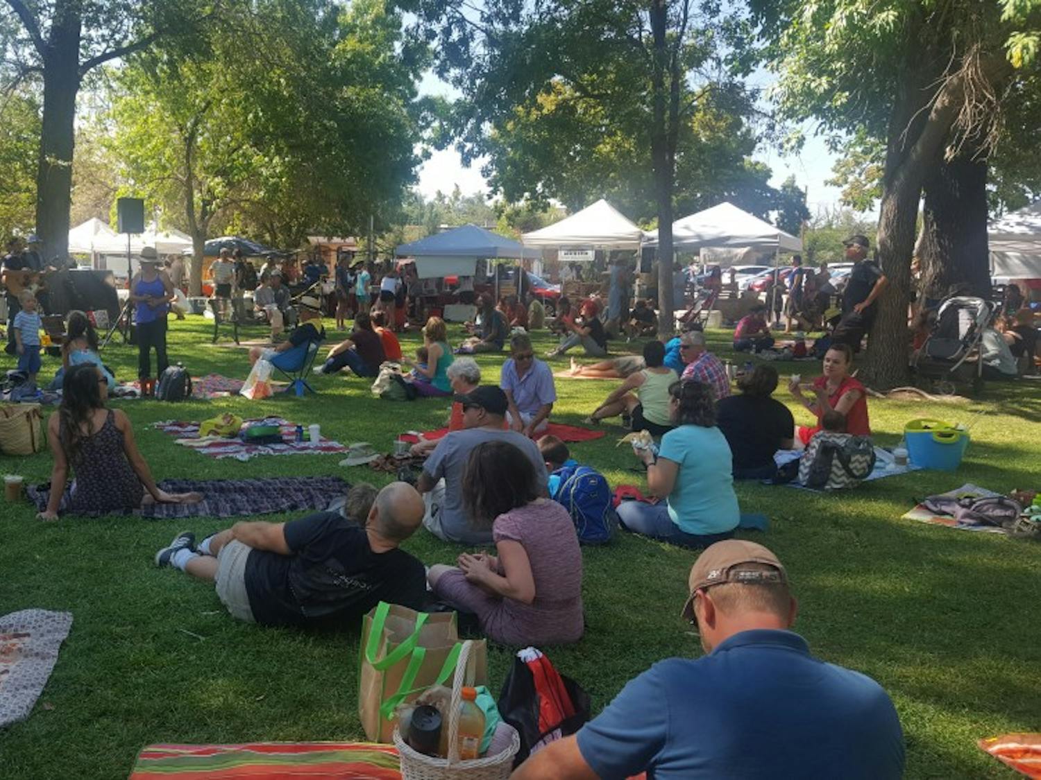 People sit and listen to a band play at the Downtown Growers Market at Robinson Park.