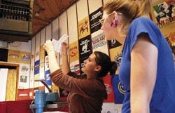Taylor Hildenbrand, left, shows new employee Diana Erickson how to print logos on shirts at the clothing store UNI on Monday.