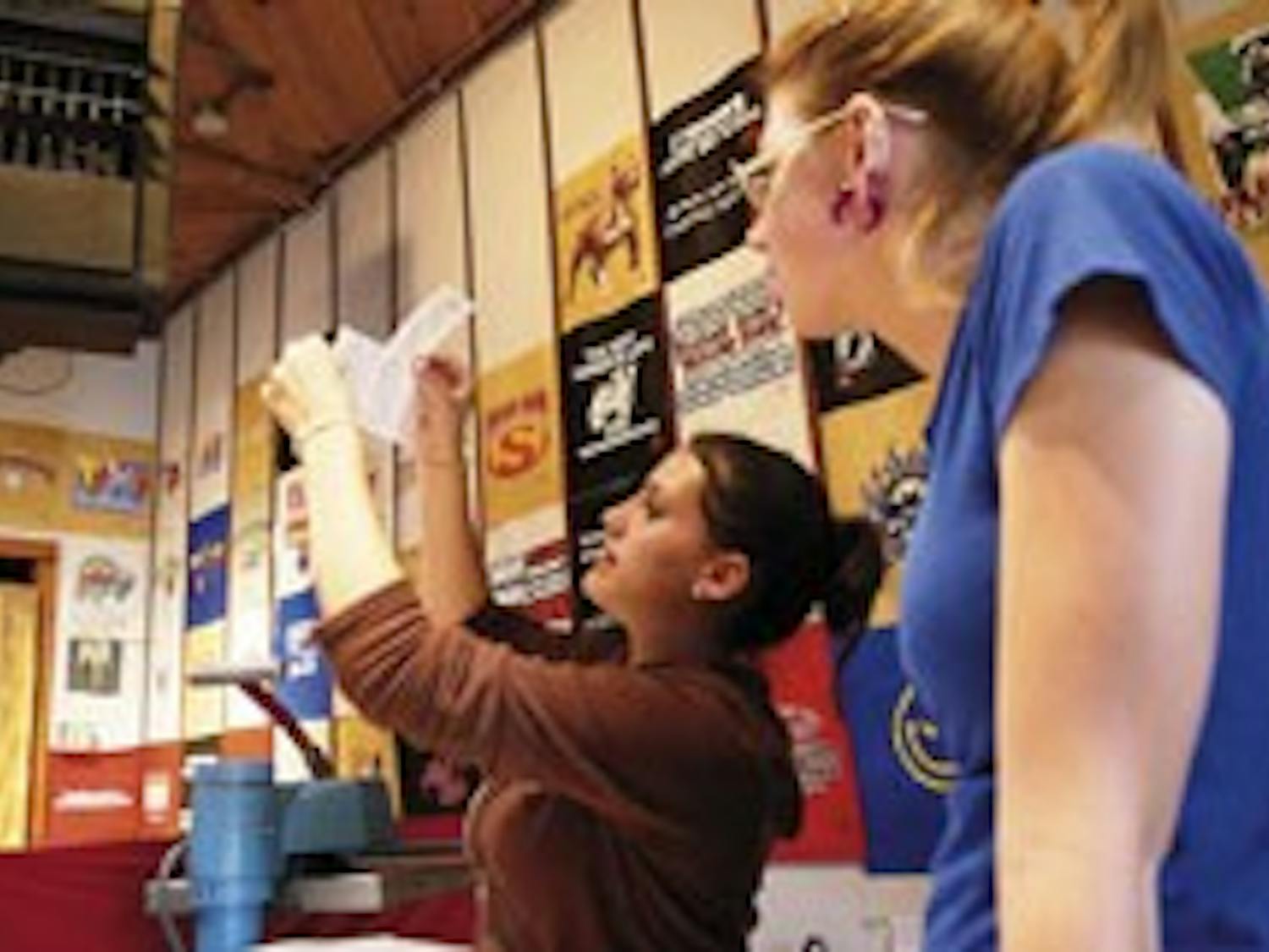 Taylor Hildenbrand, left, shows new employee Diana Erickson how to print logos on shirts at the clothing store UNI on Monday.