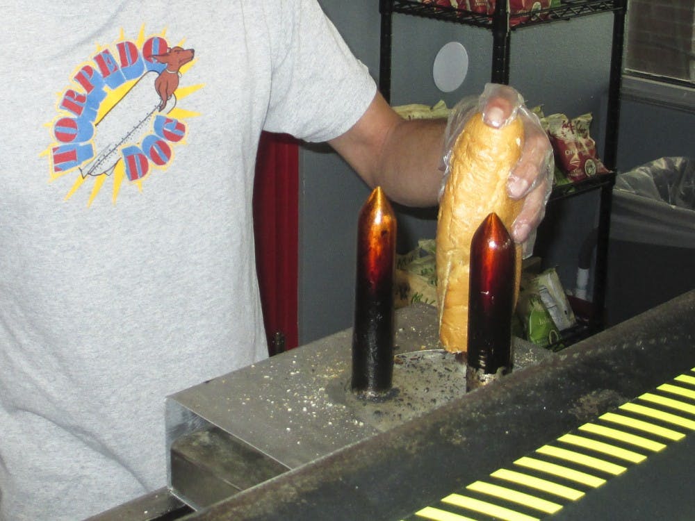 Damian Montoya, owner of Torpedo Dog, toasts the inside of a baguette on an electric spike before filling the bread with sauce and a Nathan’s hot dog or Polish sausage. 