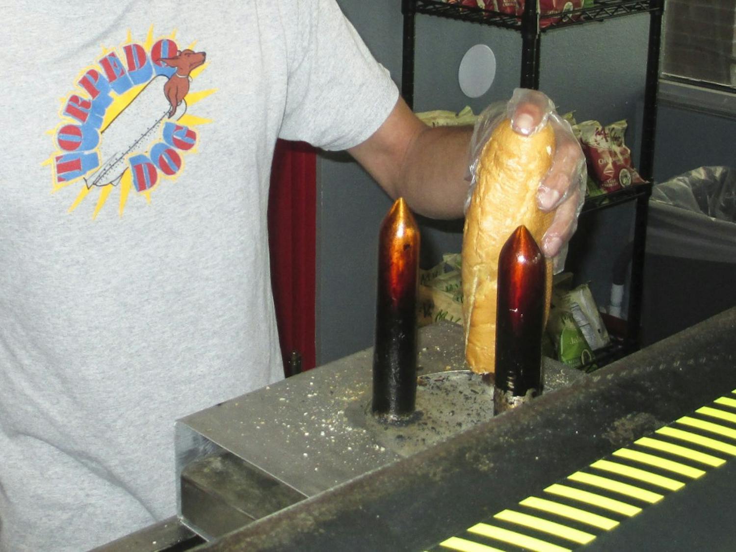 Damian Montoya, owner of Torpedo Dog, toasts the inside of a baguette on an electric spike before filling the bread with sauce and a Nathan’s hot dog or Polish sausage. 