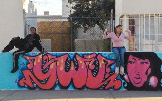 Artists Kirbie Platero, left, and Samuela Sitonik sit on a mural at Young Women United. 