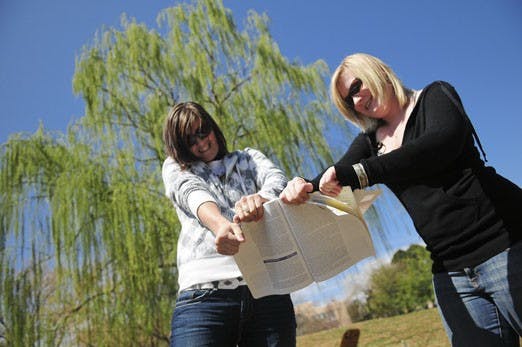 Students Angie Poss, left, and Erica Krause rip a textbook at the Duck Pond on Wednesday. The New Mexico Public Interest Research Group (NMPIRG) hosted a "Textbook Graveyard" event for students to express their anger at the Bookstore's textbook buyback po