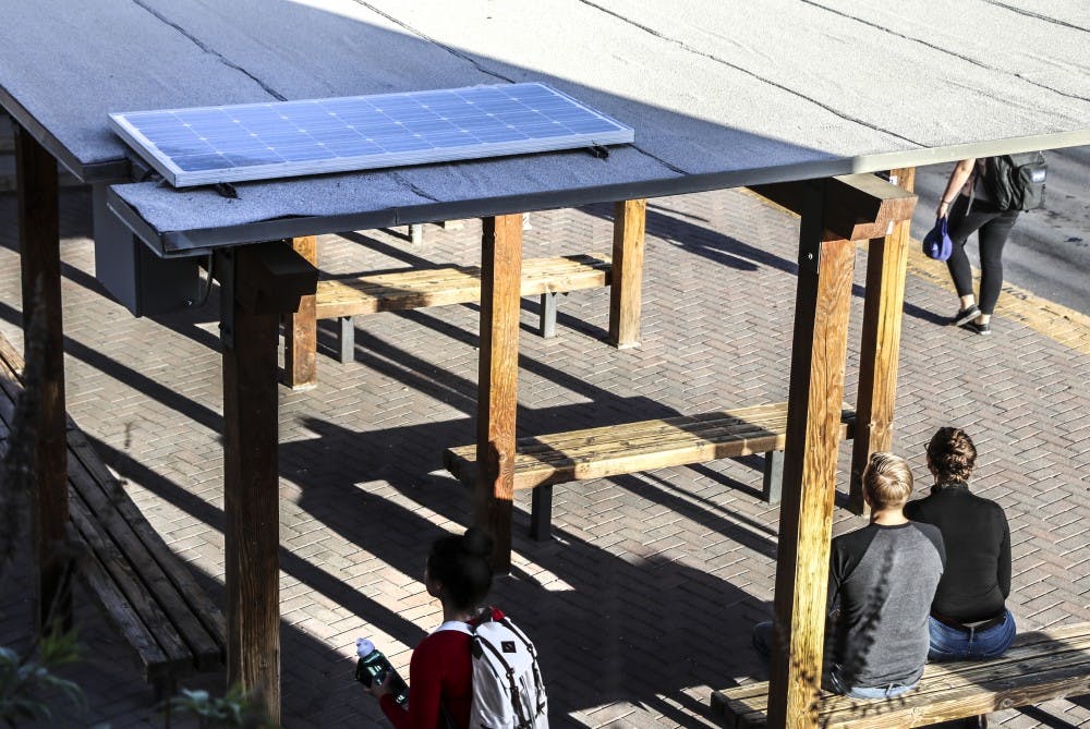 UNM students sit at the South Lot shuttle bus stop on April 18, 2018. The bus stop lights are powered by a solar panel on the roof of the stop.