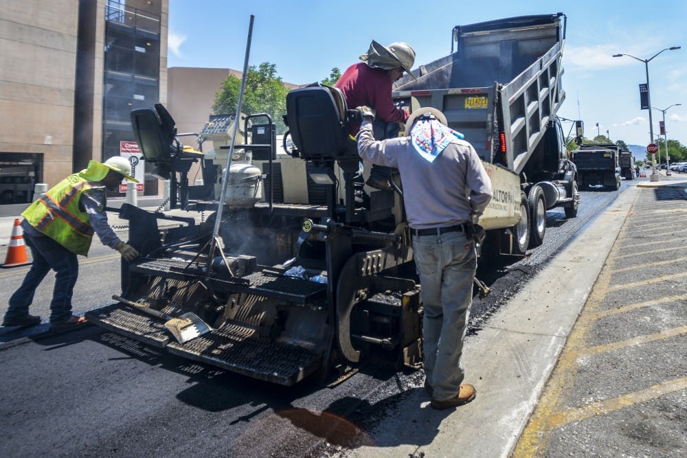 Construction workers walk and ride alongside Redondo Drive as they pour fresh asphalt on the road Thursday June 23, 2016. The project is ran by UNM’s Physical Plant Department, with hopes to improve security and sustainability around campus.