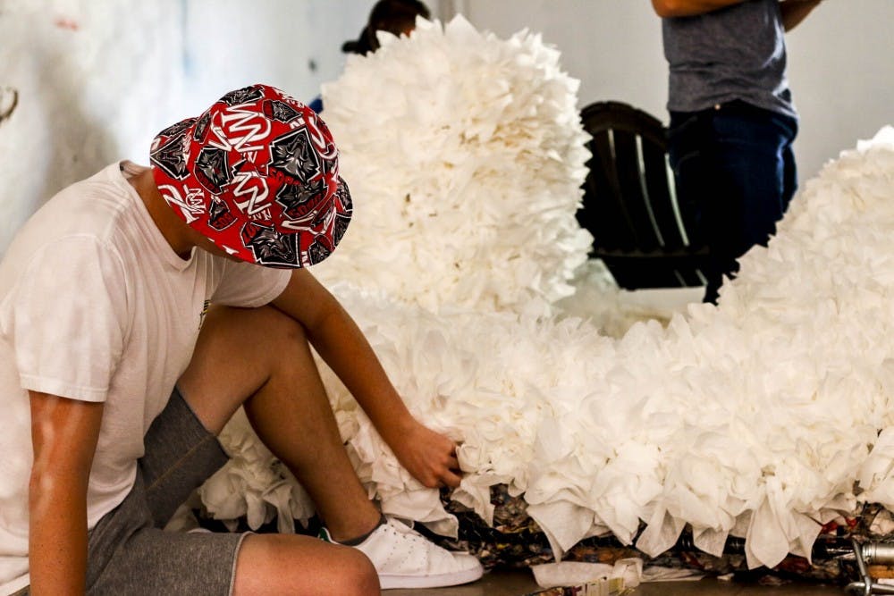 A UNM student sits next to a pile of tissues and crumbled newspapers used to build the Aggie for Red Rally on Aug. 30, 2017. The Aggie typically stands 25 feet tall and takes about 30 hours to build.