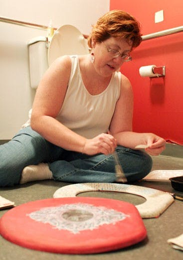 Elaine Russell, member of the Wooden Cow Gallery, decoupages WWII love letters onto a toilet seat, set to hang in the co-op's bathroom, on Monday for the "Art de Toilette" show. 