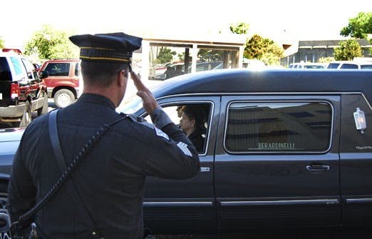 A state policeman salutes the hearse carrying Sgt. Andrew Tingwall during a procession Saturday. Tingwall piloted the helicopter that crashed last week after rescuing UNM student Megumi Yamamoto.