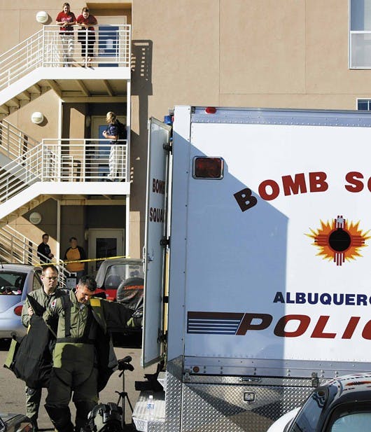 The Albuquerque Police Department's bomb squad technicians finish investigating two suspicious packages Monday, while residents of Redondo Village Apartments watch from a stairwell. 