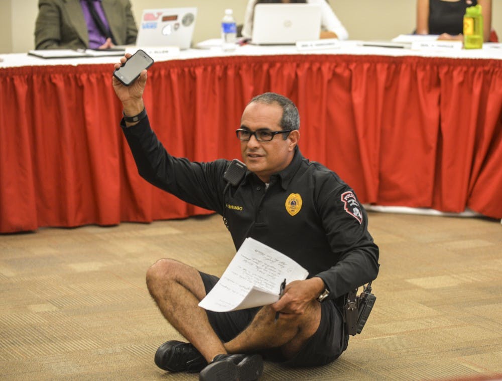 A UNM Police Department officer, Luis Santiago, demonstrates how students sit in the corners of buildings at night during ASUNM’s meeting Wednesday evening. Santiago talked about safety around campus, what students should and should not do.