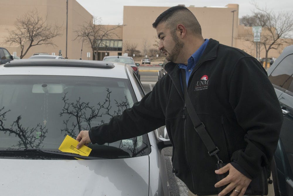 Albert Tafoya, supervisor of UNM Parking and Transportation Services, puts a parking ticket on the windshield of a car that parked without a permit at the A Lot on Monday.