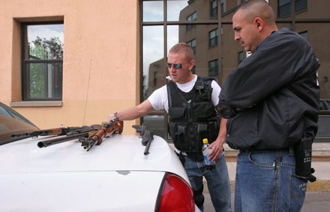 UNM Police officers Robert Rush, left, and Ernesto Pacheco look at the guns found in student Kevin Boyar's  off-campus home Tuesday. Boyar was arrested on charges of bringing weapons on campus.