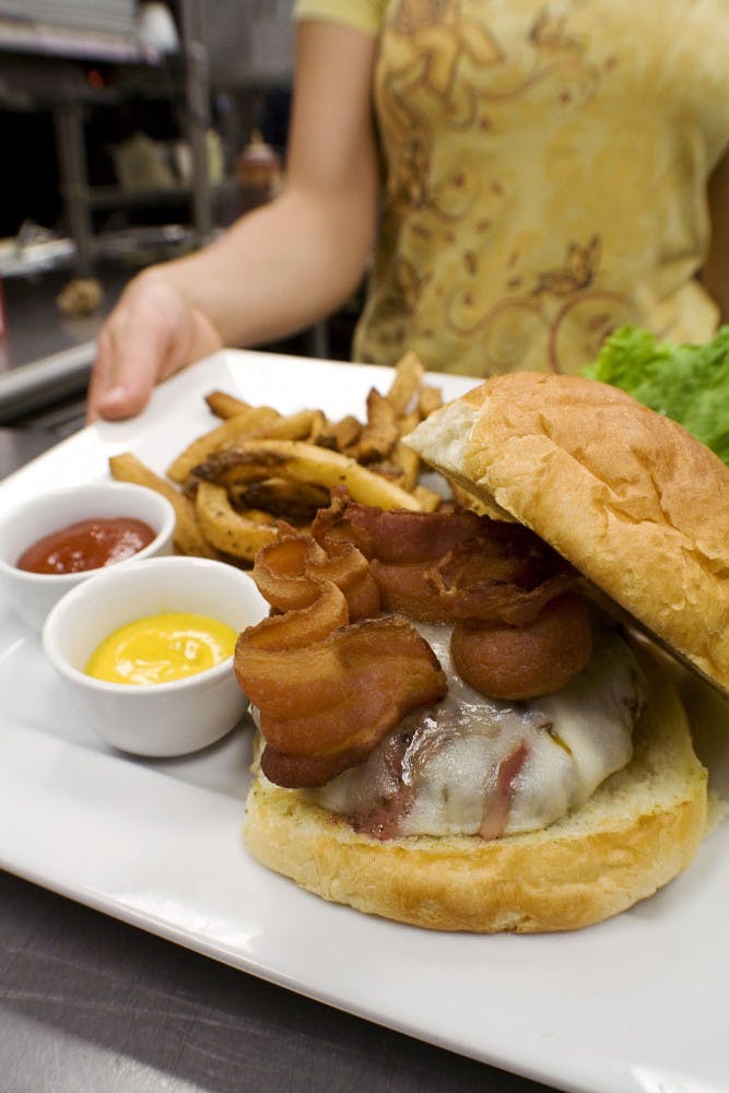 	Tasha Williams serves a 1/2 pound bacon cheeseburger at The Cube restaurant on Monday. They offer Memphis, Tenn.  – style barbecue along with other delicacies. 