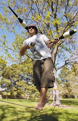 Freshman Andrew Towl juggles while walking on a slack line Tuesday at the Duck Pond. People who slack line, which is also called loose rope walking, use a nylon webbing that is taut and springy. 
