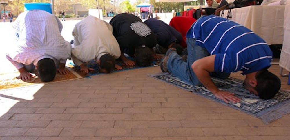 Student Imran Chiragh, right, leads a prayer at the Muslim Student Association's booth at Smith Plaza on Monday as part of Islamic Awareness Week.