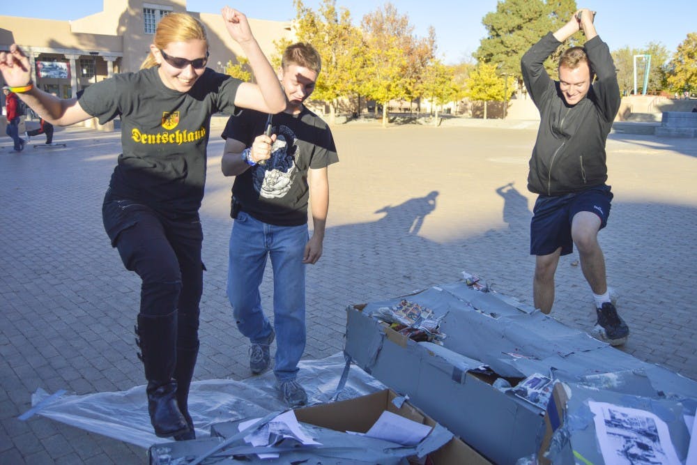 UNM biomedical engineering sophomore Lynne Tucker, left, German senior Nate Webb, center, and political science junior Torin Hovander, right, destroy a cardboard replica of the Berlin Wall outside the Humanities Building on Monday afternoon. Sunday, Nov. 9 commemorated the 25th anniversary of the Berlin Wall being brought down.