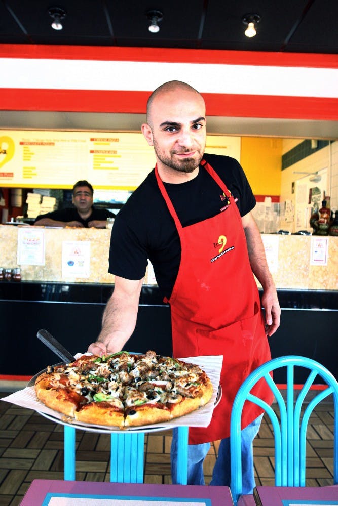 	Co-owners Hass Aslami, left, and Rod Etemadi display a deluxe pizza at Pizza 9’s Gibson location on Monday. Pizza 9 is holding their first annual pizza eating contest on Saturday.